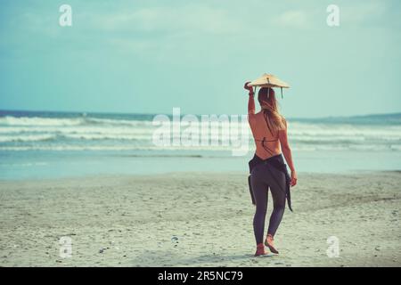 C'est un endroit où le temps est toujours là. une jeune surfeuse transportant sa planche de surf sur la plage. Banque D'Images