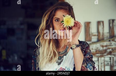 Toutes les bonnes choses sont sauvages et gratuites. Portrait d'une jeune femme libre et animée posant dans un magasin de bord de route avec une fleur. Banque D'Images