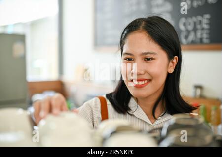 Image rapprochée d'une belle et amicale jeune femme asiatique personnel du café ou barista nettoyant et réglant la tasse de café sur un comptoir. Banque D'Images