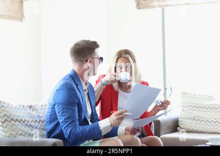 Un jeune couple discute autour d'une tasse de café dans un café et regarde à travers les documents d'affaires Banque D'Images