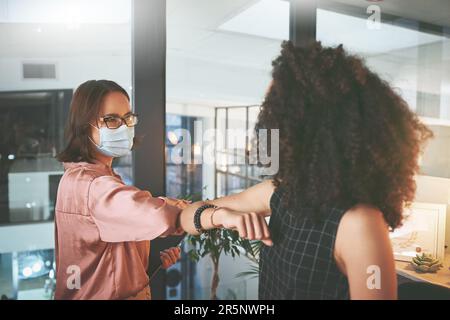 La nouvelle façon de secouer les mains. deux femmes d'affaires se tenant debout et se portant les unes les autres et portant des masques au cours d'une réunion au bureau. Banque D'Images