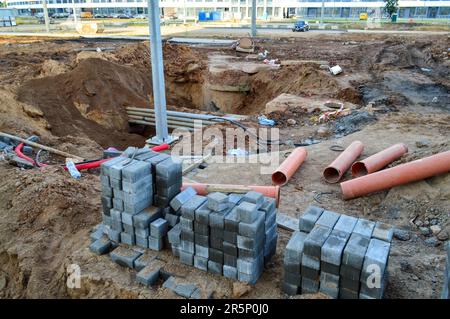 des briques d'asphalte se trouvent sur un chantier de construction. de petites briques grises sont empilées à plat sur un chantier de construction dans le centre-ville. à proximité sont des tuyaux métalliques et un Banque D'Images