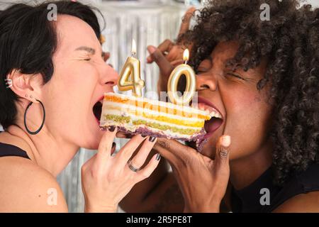 Deux femmes multiraciales mangent un gâteau avec 40 bougies d'anniversaire lors d'une fête d'anniversaire. Banque D'Images