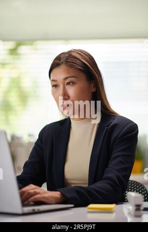 Femme entrepreneure concentrée travaillant sur ordinateur portable au bureau, vérifiant des documents et des e-mails Banque D'Images