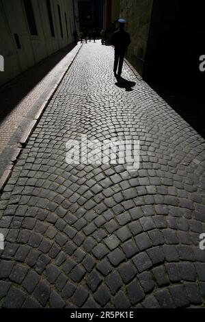 Rue pavée à Mala Strana, Prague, République tchèque, avec une figure solitaire d'un homme en uniforme bleu qui se trouve à pied Banque D'Images