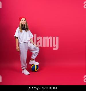 Une adolescente tient une balle de volley-ball en main et sourit sur un fond jaune rouge. Photo de studio. Banque D'Images