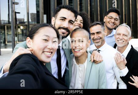 Groupe multiracial de gens d'affaires joyeux et réussis prenant un selfie à l'extérieur. Divers collègues de bureau rient en prenant une photo ensemble Banque D'Images