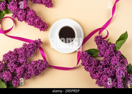 Tasse de café noir frais et branche de lilas violets fleuris avec ruban de satin sur fond orange. Pause café. Fleurs de printemps. Plan d'agencement, vue de dessus Banque D'Images