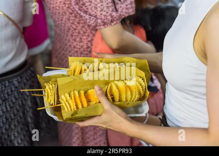 Mains tenant une boîte de papier avec frites de pommes de terre sur brochettes dans le marché nocturne vietnamien Banque D'Images