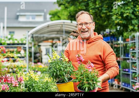 Homme d'âge moyen jardinier achetant des plantes dans le centre de jardin, tenant des pots avec le jardin jaune et rose snapdragon Banque D'Images