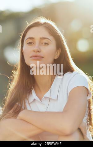 Portrait d'une jolie jeune femme avec des cheveux longs brunette et maquillage naturel posant dans un polo blanc et regardant l'appareil photo, arrière-plan flou, Miami, Banque D'Images