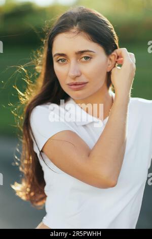 Portrait d'une jeune femme attrayante avec des cheveux longs brunette debout dans un polo blanc et regardant l'appareil photo, arrière-plan flou, Miami, Floride, ico Banque D'Images