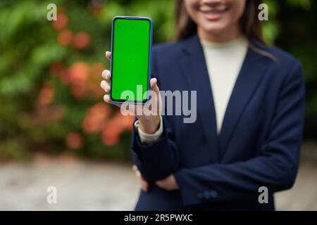 Image rognée d'une femme d'affaires montrant un smartphone avec un écran vert Banque D'Images