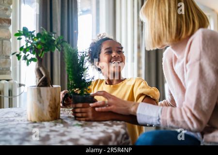 Bonne mère caucasienne et son adoption fille afro-américaine prenant soin des plantes à l'intérieur. Banque D'Images