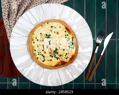 Quiche à la truite fumée, fromage de chèvre et petits pois, sur une assiette blanche, sur fond de tuile verte, vue du dessus Banque D'Images