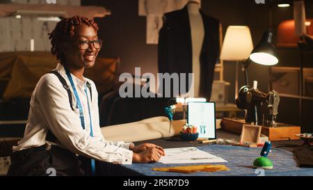 Le couturier féminin travaille sur la conception de vêtements, en regardant des croquis pour créer une ligne de vêtements de luxe à l'atelier de travail. Personnalisez les articles faits à la main des employés pour une collection d'ateliers de luxe. Banque D'Images