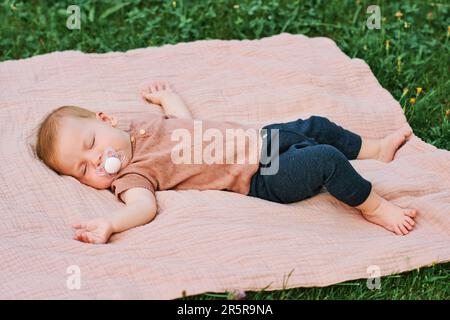 Portrait d'un bébé doux dormant à l'extérieur, d'un enfant qui se couche sur une couverture dans le jardin ou dans le parc Banque D'Images