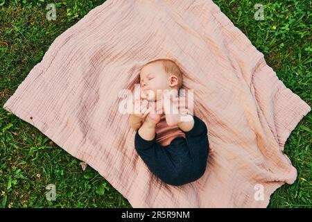 Portrait de bébé doux jouant à l'extérieur, enfant appréciant l'air frais sur une couverture dans le jardin ou le parc Banque D'Images