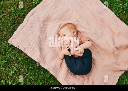 Portrait de bébé doux jouant à l'extérieur, enfant appréciant l'air frais sur une couverture dans le jardin ou le parc Banque D'Images