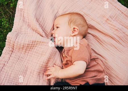 Portrait de bébé doux jouant à l'extérieur, enfant appréciant l'air frais sur une couverture dans le jardin ou le parc Banque D'Images