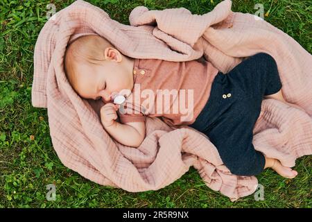 Portrait de bébé doux jouant à l'extérieur, enfant appréciant l'air frais sur une couverture dans le jardin ou le parc Banque D'Images