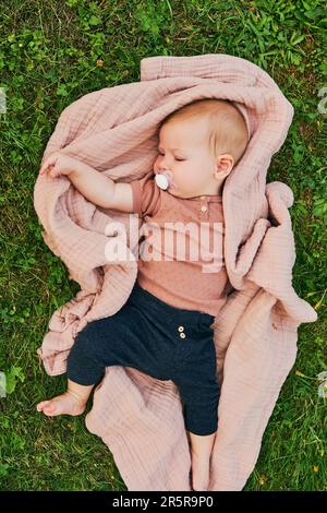 Portrait de bébé doux jouant à l'extérieur, enfant appréciant l'air frais sur une couverture dans le jardin ou le parc Banque D'Images