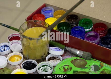 photo ouverte avec différentes couleurs de peintures et pinceaux et un verre d'eau sale Banque D'Images