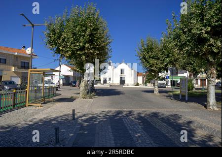 Quiaios, Portugal - 14 août 2022: Vue sur la rue montrant la route bordée d'arbres, arrêt de bus, église avec passage en croix en premier plan Banque D'Images