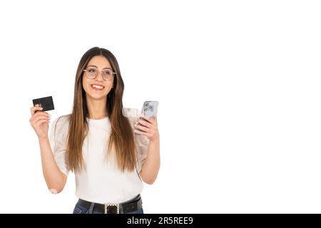 Concept de paiement en ligne jeune fille excité. Femme brune adolescente tenant une carte de crédit en plastique noir et un téléphone portable moderne sur ses mains. Banque D'Images