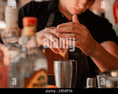 Un barman professionnel crée des cocktails uniques dans un bar, avec une variété de différentes boissons alcoolisées exposées en arrière-plan Banque D'Images