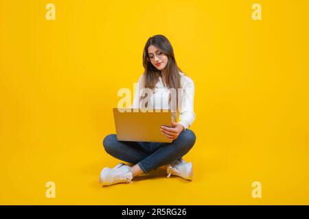 vue sur le corps une femme assise au sol travaillant sur un ordinateur portable. Jeune femme d'affaires caucasienne tenant un ordinateur portable sur ses genoux. Banque D'Images