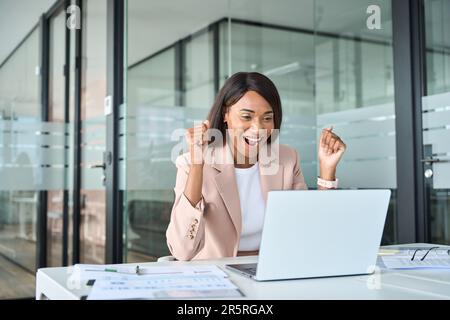 Une jeune femme d'affaires enthousiaste qui regarde un ordinateur portable pour fêter son succès financier. Banque D'Images