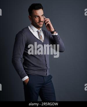 Le gars à appeler pour conclure la transaction. Photo studio d'un jeune homme d'affaires élégant utilisant un téléphone portable sur fond gris. Banque D'Images