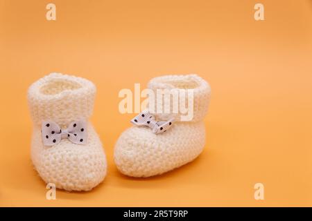 Chaussons blancs tricotés pour bébé avec noeuds à pois sur fond isolé orange. Arrière-plan. Pour le texte. Photo de haute qualité Banque D'Images