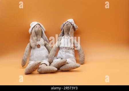Des lapins en tilde faits main dans des vêtements blancs pour décorer la maison sur un fond pêche pour décorer l'appartement. Photo de haute qualité. Horizontale. Banque D'Images