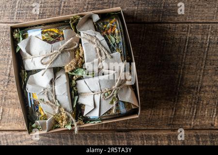 Quatre bocaux en verre avec fleurs sèches et tisane dans une boîte cadeau sur fond de bois, espace de copie, vue de dessus. Tisane Banque D'Images