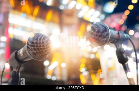 Deux microphones professionnels sur un stand noir sur fond de rue avec des lumières floues de différentes couleurs Banque D'Images