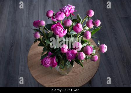 Un bouquet de pivoines est placé dans un vase sur une table ronde en bois Banque D'Images