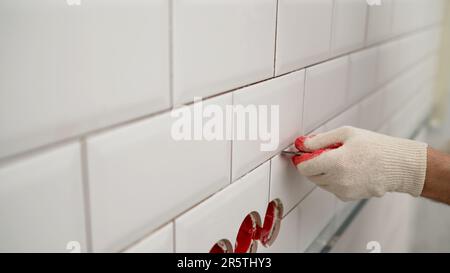 Nettoyage des coutures des carreaux de céramique. Coutures entre les carreaux dans la cuisine. Un homme utilise un couteau pour enlever la saleté. Remplacer le vieux coulis entre les carreaux. Nettoyage Banque D'Images