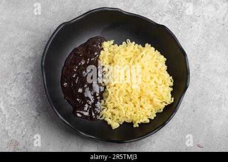 Nouilles instantanées coréennes Jajangmyeon ou Jajangmyeon dans une tasse noire avec sauce noire. Banque D'Images