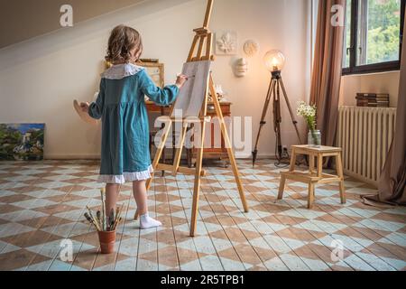 une petite fille mignonne tire derrière un chevalet. rêvant Banque D'Images