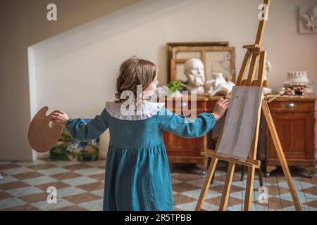 une petite fille mignonne tire derrière un chevalet. rêvant Banque D'Images