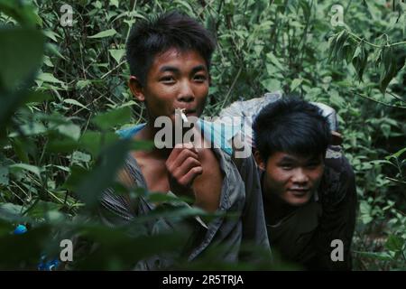 Deux jeunes garçons, amis, vivant dans le moment, en appréciant une cigarette, tout en étant engloutis et encadrés par la jungle sauvage. Banque D'Images