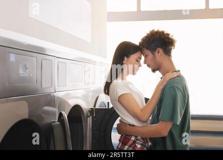 Couple mixte aimant se tenant près des lave-linge de la laverie automatique intérieur Banque D'Images