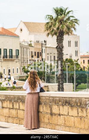 Fille de cheveux rouges marchant sur les murs anciens avec la basilique pontificale ou l'église Saint-Nicolas et des palmiers sur fond dans la vieille ville de Bari, Puglia Banque D'Images