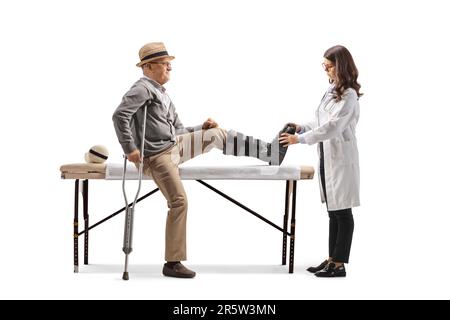 Homme âgé avec un étrésillon de jambe assis sur un lit et une femme médecin vérifiant son pied isolé sur fond blanc Banque D'Images