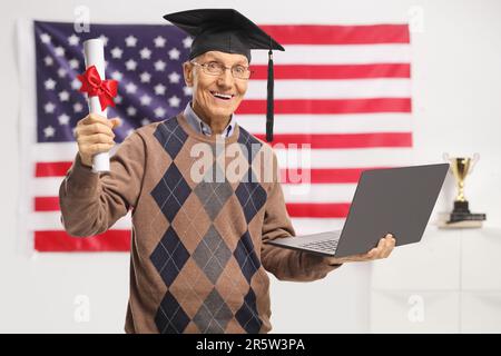 Homme senior titulaire d'un diplôme et d'un ordinateur portable devant un drapeau américain Banque D'Images