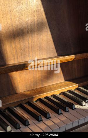 Un piano droit ancien debout dans une salle lumineuse éclairée par le soleil Banque D'Images