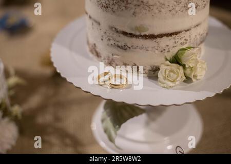 Un gâteau de mariage blanc brillant avec deux anneaux de mariage dorés Banque D'Images