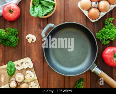 Idée pour le petit déjeuner. Videz la poêle en fonte et les ingrédients pour omelette ou œufs brouillés. Oeufs, champignons, tomates, épinards et persil sur bois Banque D'Images